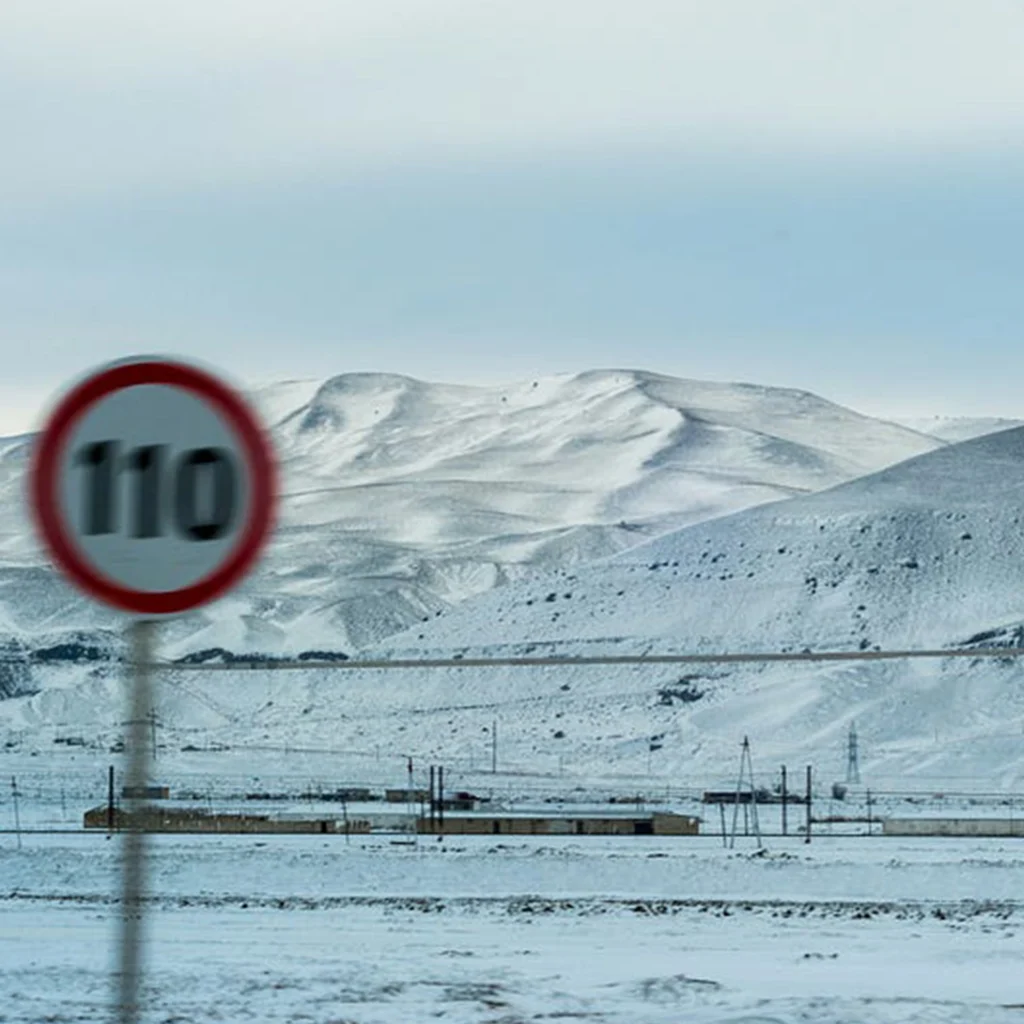 A snowy, remote landscape with a speed limit sign indicating 110 kilometers per hour, suggesting a road through the mountains.